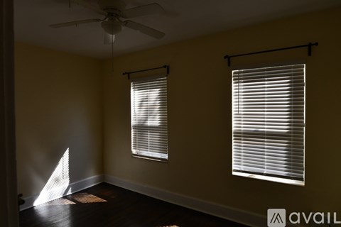 A room with a ceiling fan and two windows with blinds.