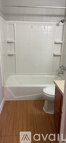 A bathroom with a toilet, tub, and wooden floor.