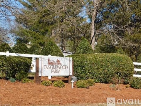 A sign that says Tanglewood Farm is in front of a white fence.