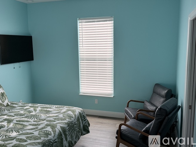 A bedroom with a bed, chair, and window with blinds.
