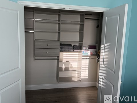 A white closet with shelves and drawers is open to a room with a window.