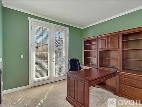 A room with green walls and a wooden desk with a black chair.