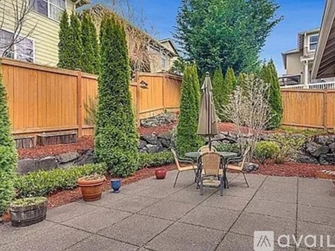 A patio with a table and chairs surrounded by a wooden fence and green plants.