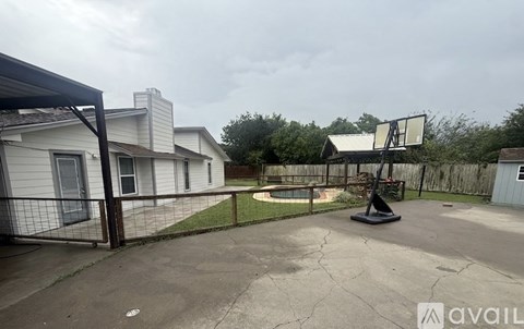 A basketball court is located in a backyard with a basketball hoop and a fence.