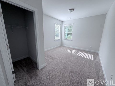 A room with a carpeted floor, a window with blinds, and a door open to another room.