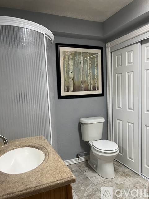A bathroom with a toilet, sink, and a picture of trees on the wall.