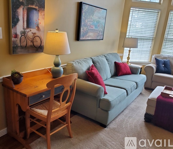 A living room with a grey couch, a wooden table with a plant and a lamp on it, and two framed pictures on the wall.