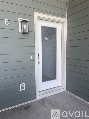 A white door with a glass window is on the right side of a wall with a light switch and a letter B on the left.