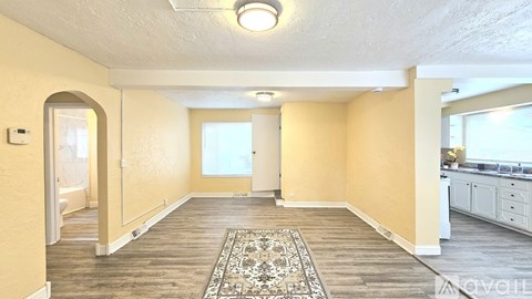 A spacious room with a rug in the middle and a kitchen area to the right.