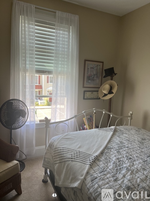 A bedroom with a bed, fan, and window with curtains.