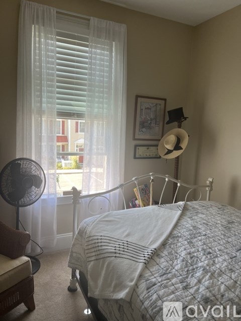 A bedroom with a bed, fan, and window with curtains.
