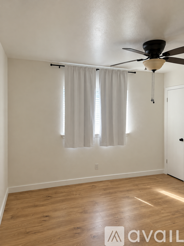 A room with a ceiling fan and a window with curtains.