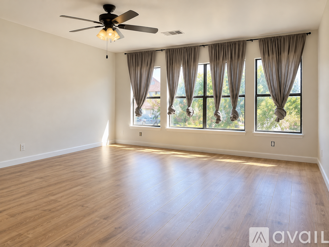 A room with a ceiling fan and large windows with curtains.