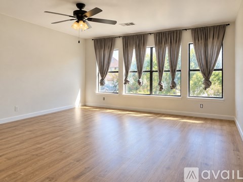 A room with a ceiling fan and large windows with curtains.