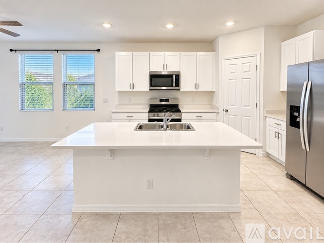 A kitchen with white cabinets and appliances, a large island, and a ceiling fan.