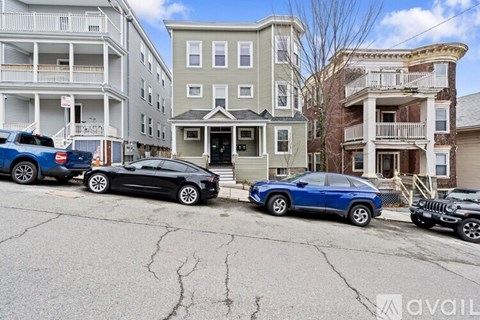 A black car is parked in front of a grey building with a sign that reads "available".