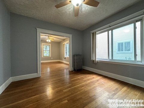 A spacious room with wooden floors and a ceiling fan.