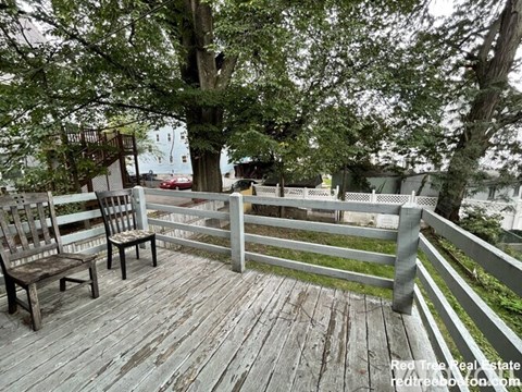 Two chairs are on a wooden deck with a fence and trees in the background.