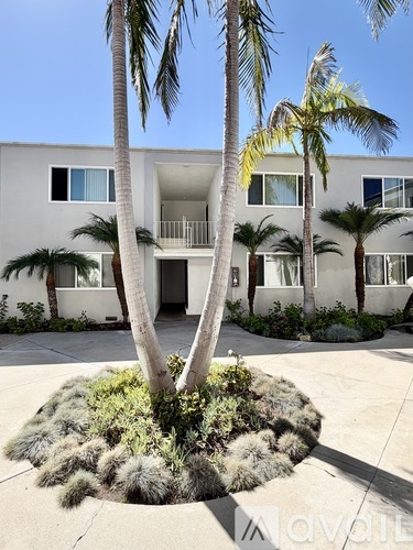 A white building with a balcony is surrounded by palm trees.