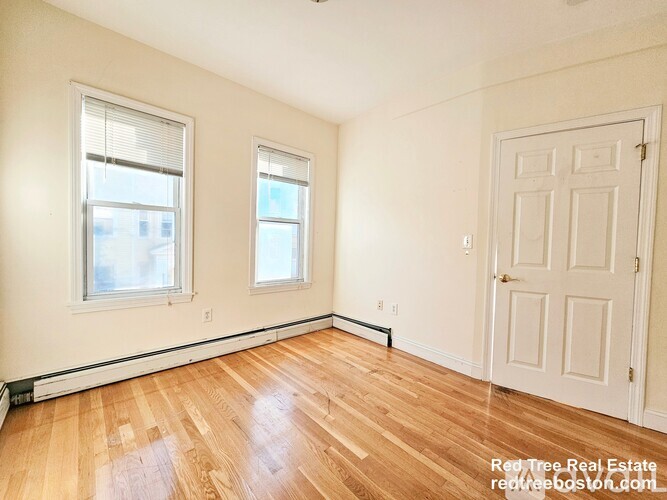 A room with wooden floors and white walls has two windows and a door.