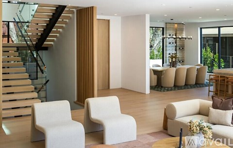 A living room with white chairs and a glass staircase.