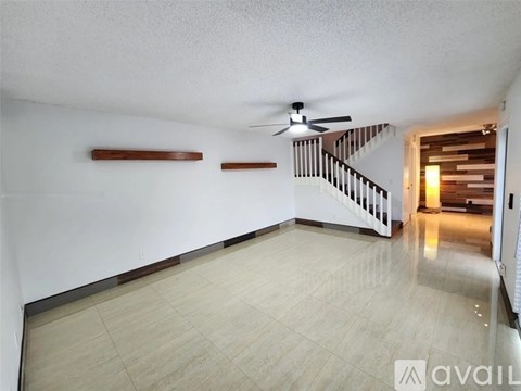 A spacious room with a fan and a staircase.