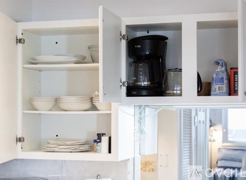A kitchen cabinet with a coffee maker and plates.