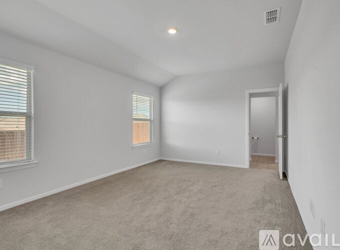 A spacious room with a carpeted floor, a window with blinds, and a door leading to another room.