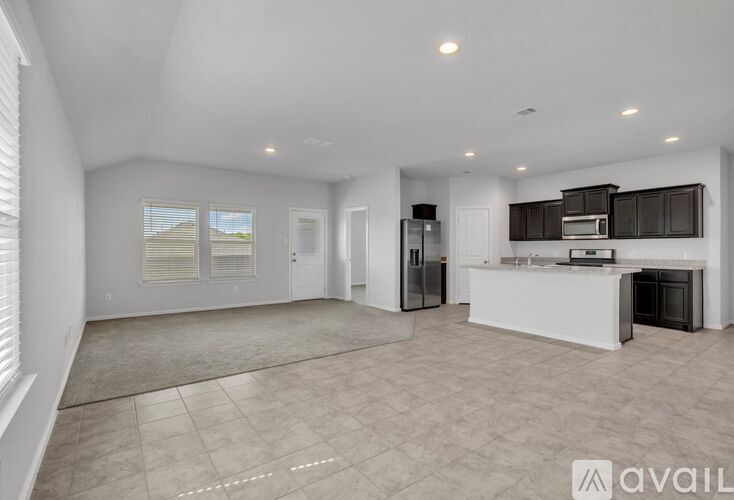 A spacious, empty living area with a kitchen in the background.