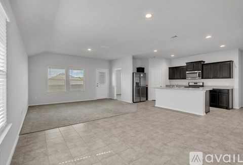 A spacious, empty living area with a kitchen in the background.