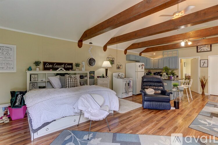 A bedroom with a large bed and a kitchen area in the background.
