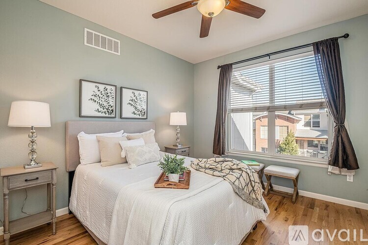 A bedroom with a bed, two lamps, a ceiling fan, and a window with a view of a building outside.