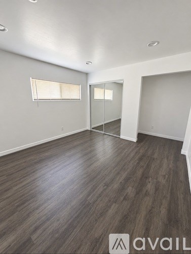 A room with wooden flooring and two windows.