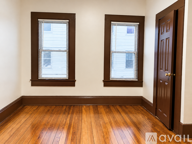 A room with wooden floors and two windows with blinds.