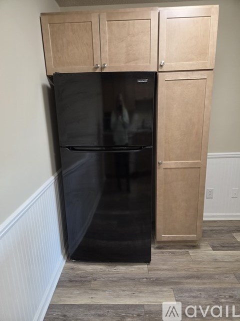 A black refrigerator with wooden cabinets on top.