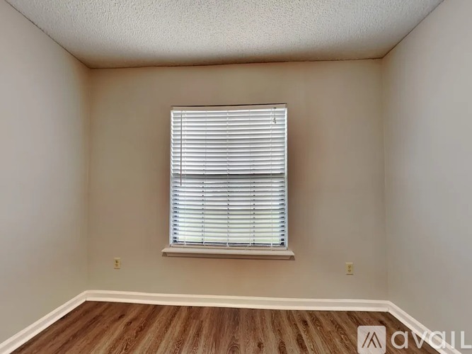 A room with a window covered by white blinds and wooden flooring.