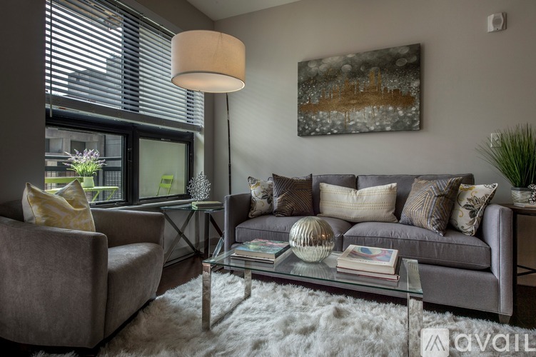 A modern living room with a grey sofa, a glass coffee table, and a large painting on the wall.