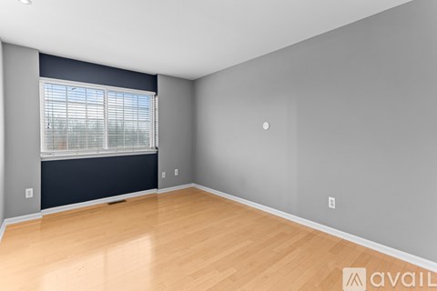 A spacious room with wooden flooring and a window with blinds.