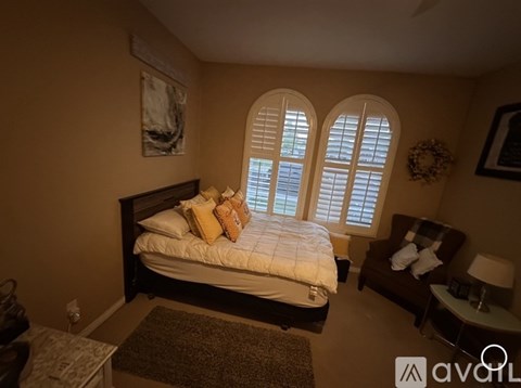 A bedroom with a bed, a chair, and a window with shutters.