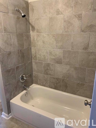 A white bathtub in a bathroom with grey tiled walls.