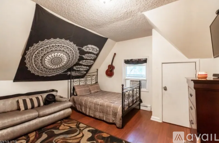 A room with a bed, a couch, and a guitar hanging on the wall.