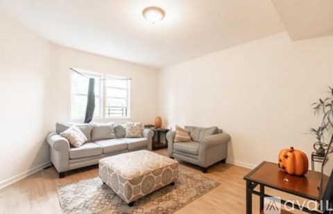 A living room with a grey couch, a white ottoman, and a small table with a pumpkin on it.