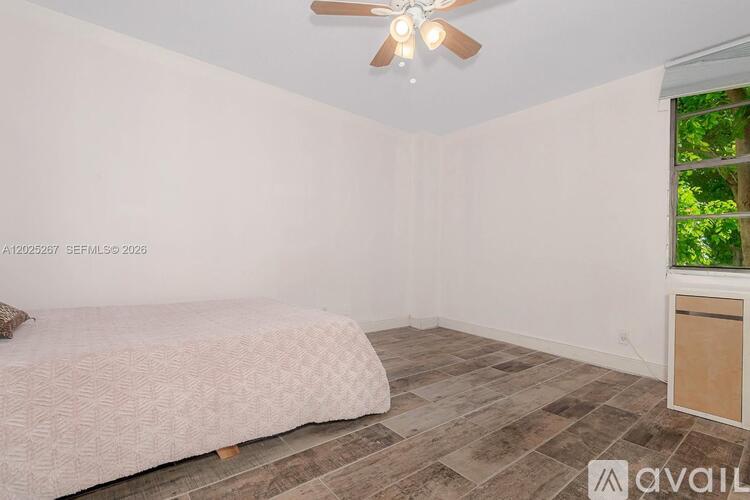 A room with a bed, a ceiling fan, and a window with a view of trees.