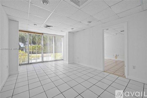 A spacious room with white tiled flooring and a sliding glass door leading to a balcony.
