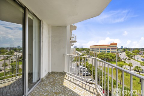 A balcony with a metal railing and a tiled floor overlooks a parking lot and buildings.