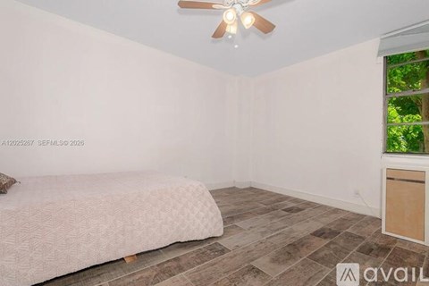 A room with a bed, a ceiling fan, and a window with a view of trees.