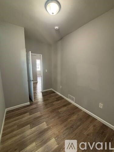 A room with wooden flooring and a doorway leading to another room.