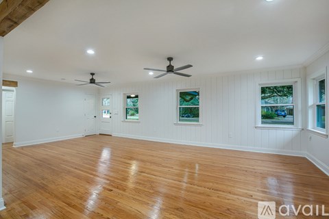 A spacious room with wooden floors and two ceiling fans.
