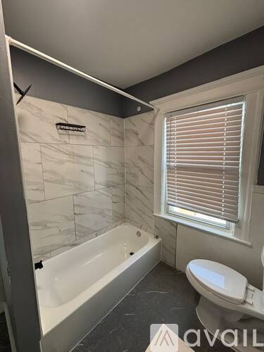 A white bathroom with a tub, toilet and window.