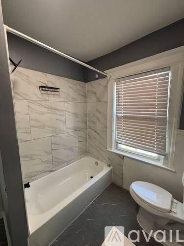 A white bathroom with a tub, toilet and window.